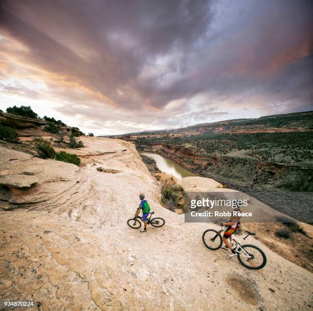 two men riding mountain bikes on an extreme sandstone ledge - robb reece stock-fotos und bilder