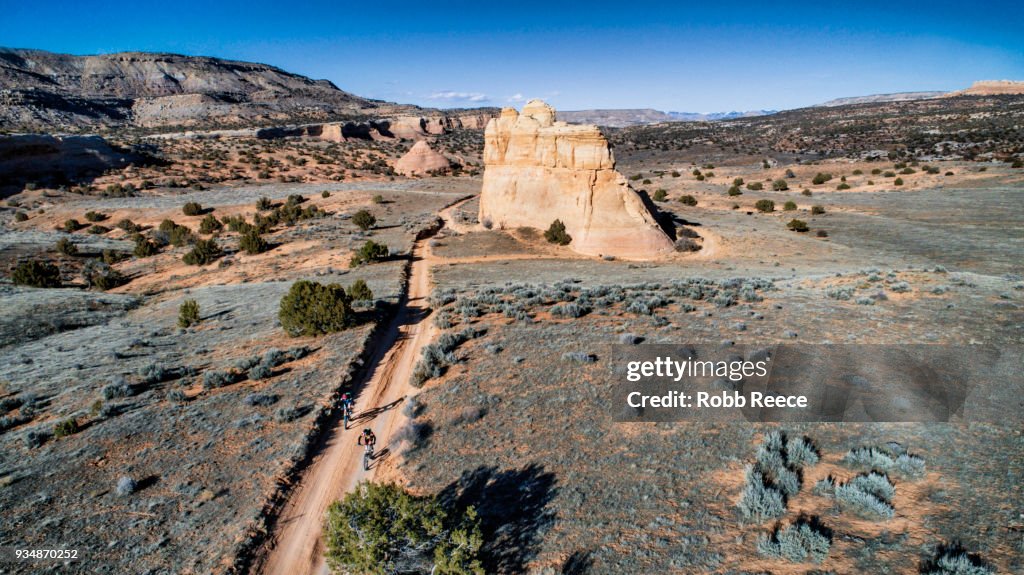 Two men riding a mountain bike on a sandy trail in the desert