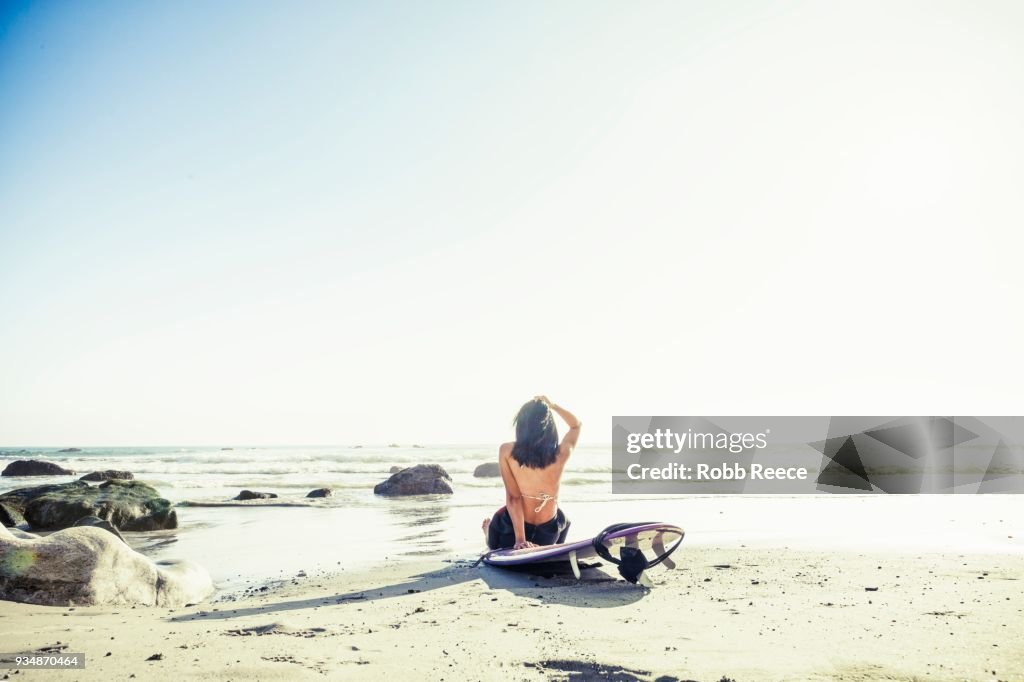 A woman surfer with a surfboard on a remote ocean beach