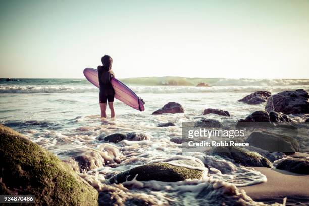 a woman surfer with a surfboard on a remote ocean beach - robb reece fotografías e imágenes de stock