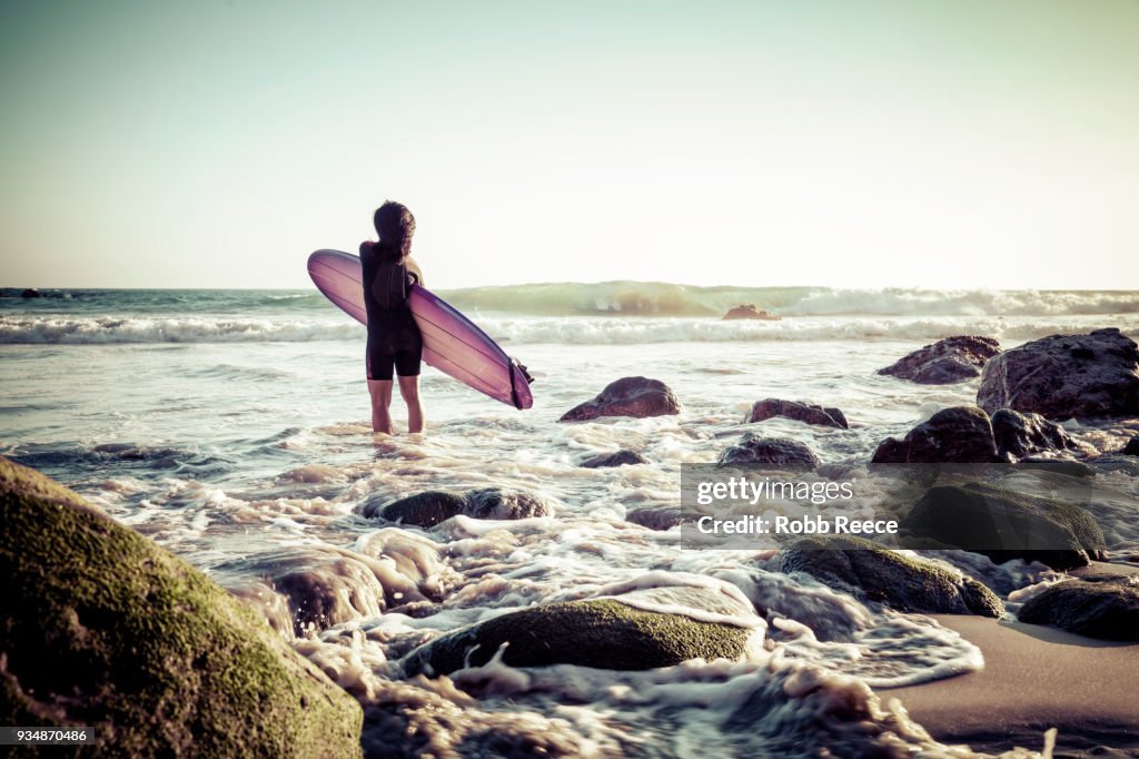 A woman surfer with a surfboard on a remote ocean beach