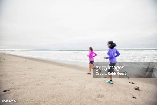 two adult woman running in the sand on a remote beach - robb reece stock-fotos und bilder
