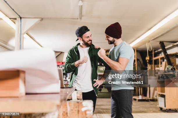 two happy young men with laptop in workshop - fist celebrating fotografías e imágenes de stock