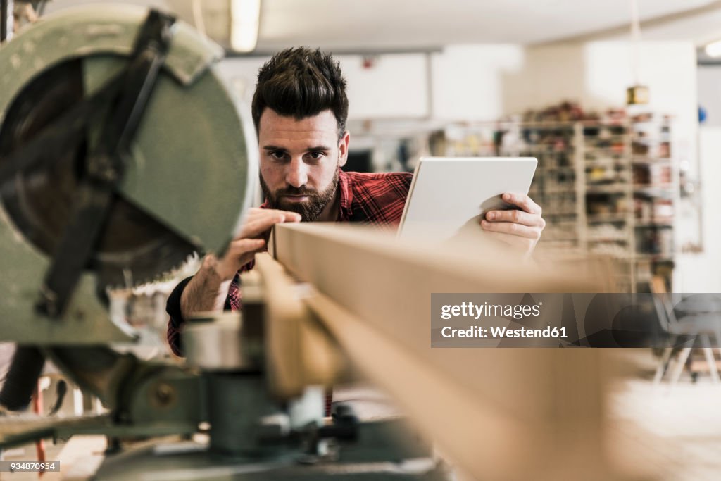 Man in workshop with piece of wood and tablet