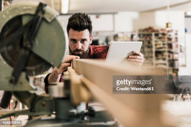 man in workshop with piece of wood and tablet - wood worker posing stock-fotos und bilder