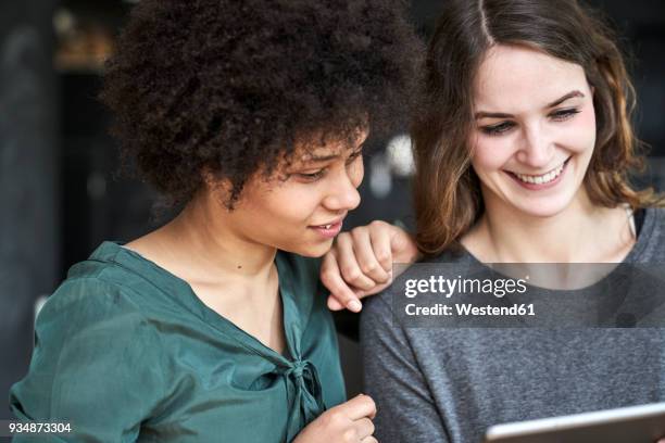 two smiling young women sharing tablet - hand auf der schulter stock-fotos und bilder