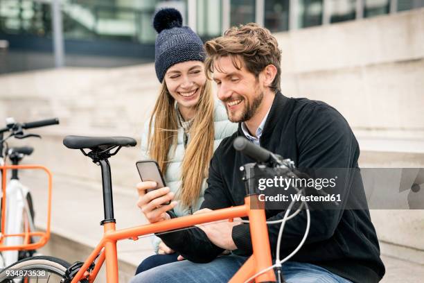 smiling couple with bicycles and cell phone in the city - fahrrad frau außen lächeln stock-fotos und bilder