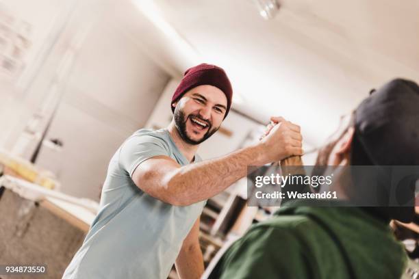 two happy young men high fiving in workshop - engagement stock-fotos und bilder