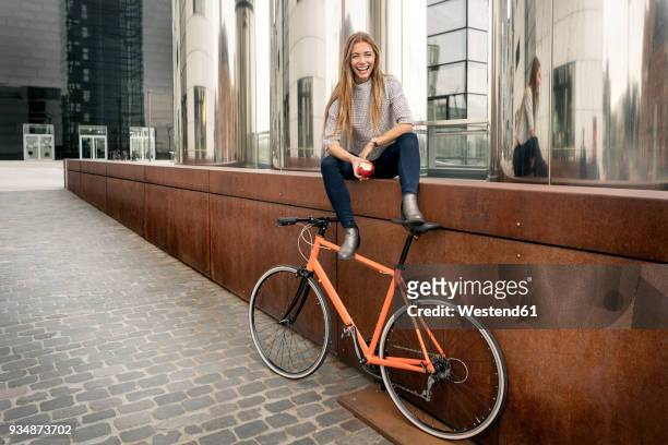 happy young woman with bicycle having a break in the city eating an apple - woman bicycle stock pictures, royalty-free photos & images