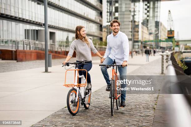 smiling couple riding bicycle in the city - verkehrsweg für fußgänger stock-fotos und bilder