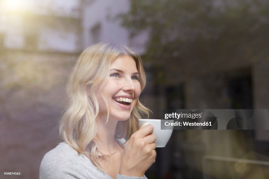 Portrait of laughing woman with cup of coffee behind windowpane