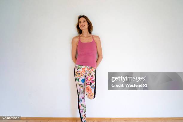 smiling mature woman leaning against a wall - floral pattern pants stockfoto's en -beelden