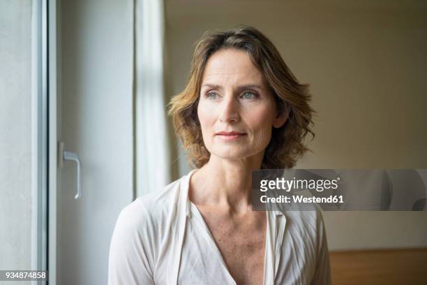 portrait of pensive mature woman at the window - white blouse stock-fotos und bilder
