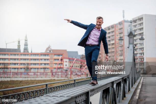 stylish mature businessman wearing blue suit balancing on railing of bridge - risk bildbanksfoton och bilder