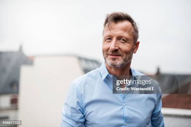 portrait of smiling mature businessman on roof terrace - blue shirt fotografías e imágenes de stock