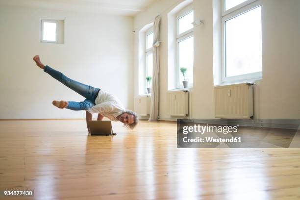 mature man doing a handstand on floor in empty room looking at tablet - acrobate photos et images de collection