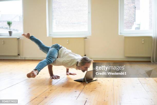 mature man doing a handstand on floor in empty room looking at tablet - male gymnast photos et images de collection