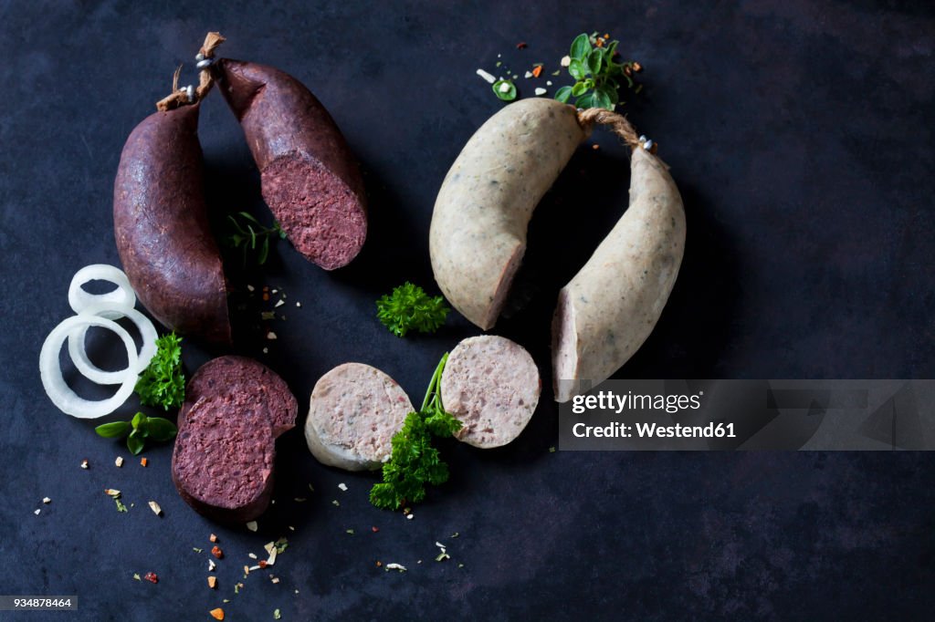 Sliced liver sausages and blood sausages, onion rings, parsley and herbs on dark ground