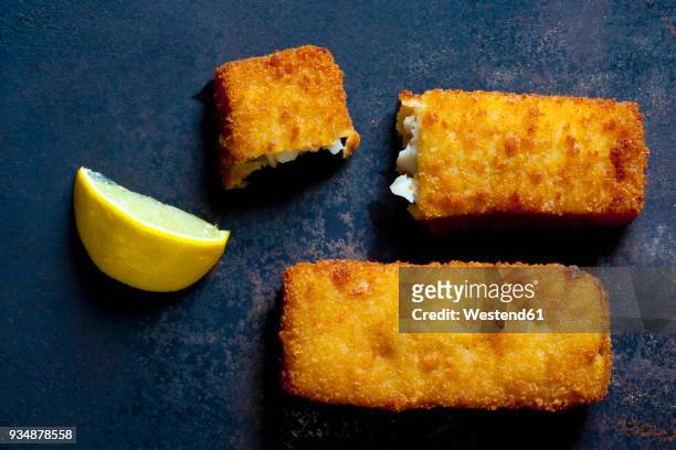 fish fingers and lemon slice on dark metal - peixe à milanesa imagens e fotografias de stock