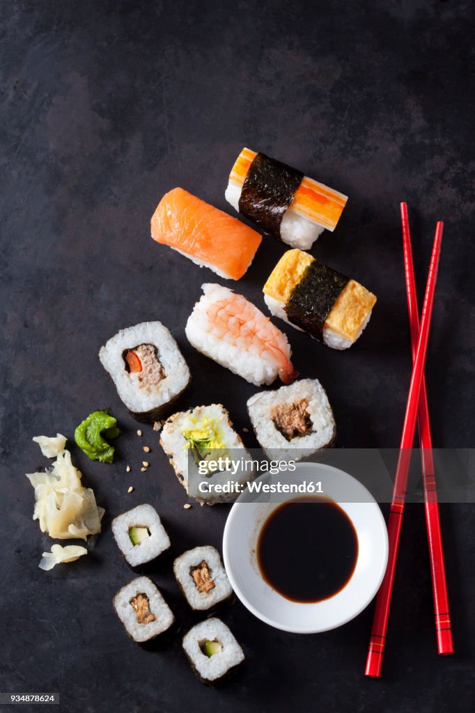 Variety of sushi with wasabi, ginger and bowl of soy sauce on dark ground