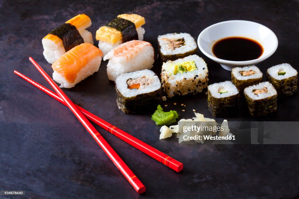 Variety of sushi with wasabi, ginger and bowl of soy sauce on dark ground