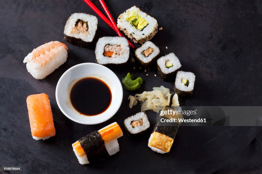 Variety of sushi with wasabi, ginger and bowl of soy sauce on dark ground