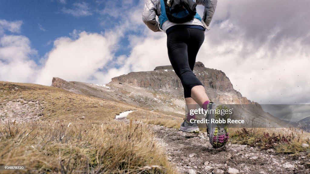 An adult woman trail running on a remote mountain trail