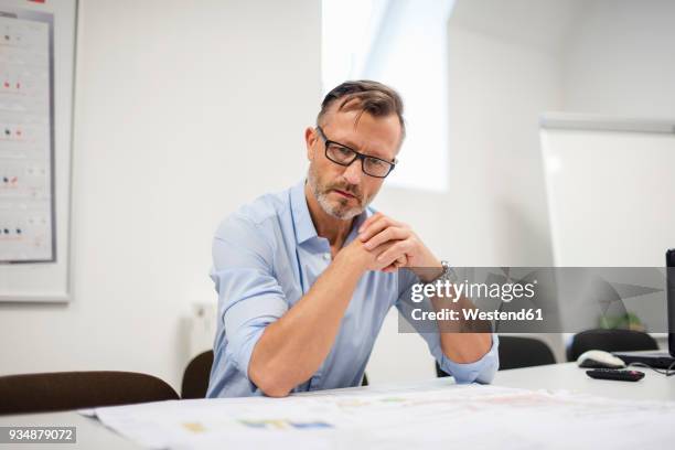 mature businessman looking at plan on desk in office - guardare verso il basso foto e immagini stock