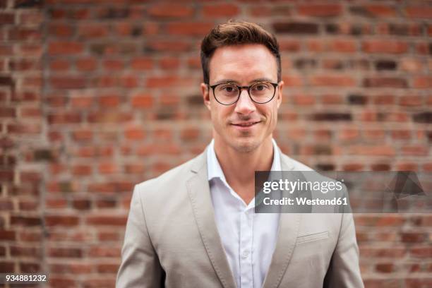 portrait of smiling young businessman at brick wall - white jacket 個照片及圖片檔