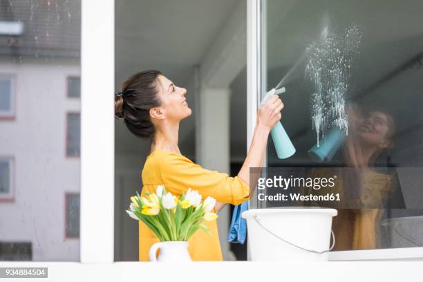 smiling woman at home cleaning the window - putzeimer stock-fotos und bilder