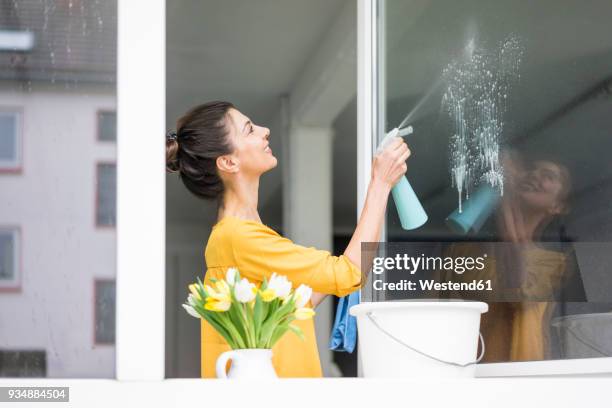 smiling woman at home cleaning the window - daily bucket photos et images de collection