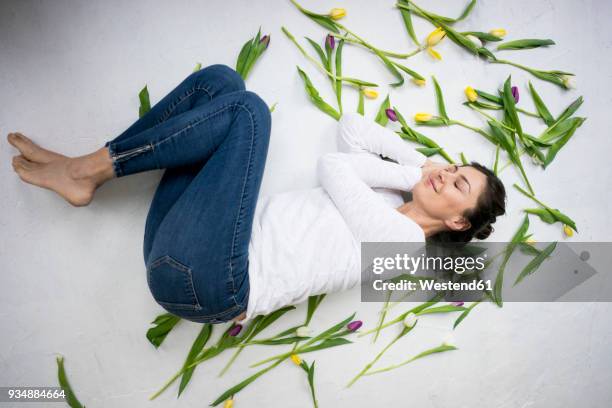 smiling woman lying on floor amidst tulips - frühjahrsmüdigkeit frau stock-fotos und bilder