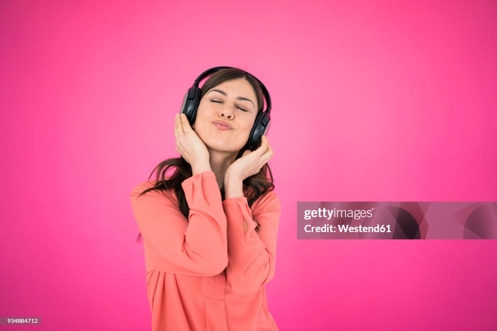 Woman in front of pink wall listening to music on headphones