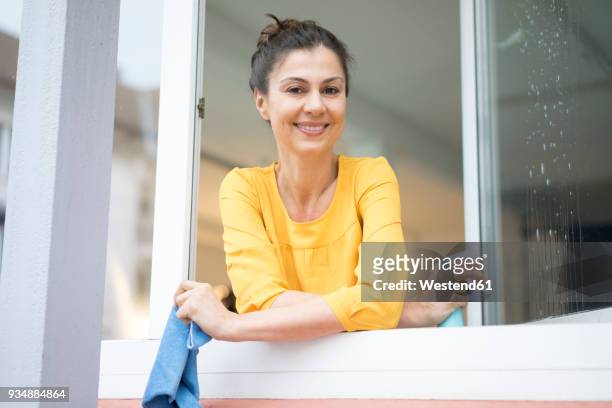 portrait of smiling woman cleaning the window - frau putzen stock-fotos und bilder