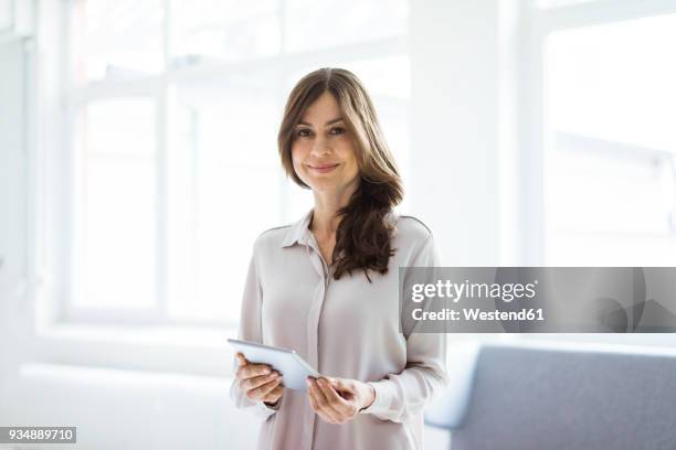 portrait of smiling woman standing in bright room holding tablet - smiling person white shirt stockfoto's en -beelden