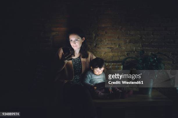 mother and daughter using cell phone and digital tablet at home in the dark - blind spot stock pictures, royalty-free photos & images