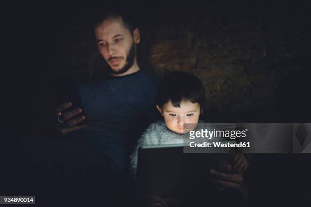 father and daughter using phablet and digital tablet at home in the dark - ignorance stock pictures, royalty-free photos & images
