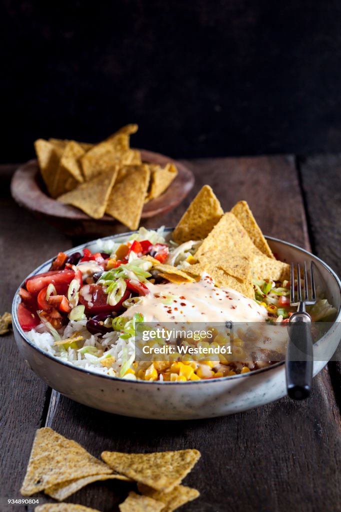 Taco salad bowl with rice, corn, chili con carne, kidney beans, iceberg lettuce, sour cream, nacho chips, tomatoes