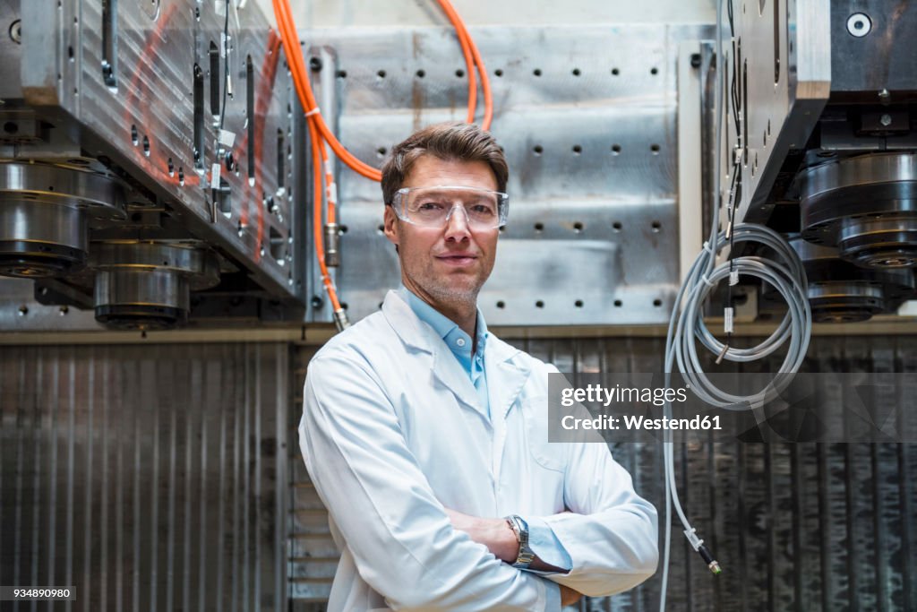 Portrait of man wearing lab coat and safety goggles at machine