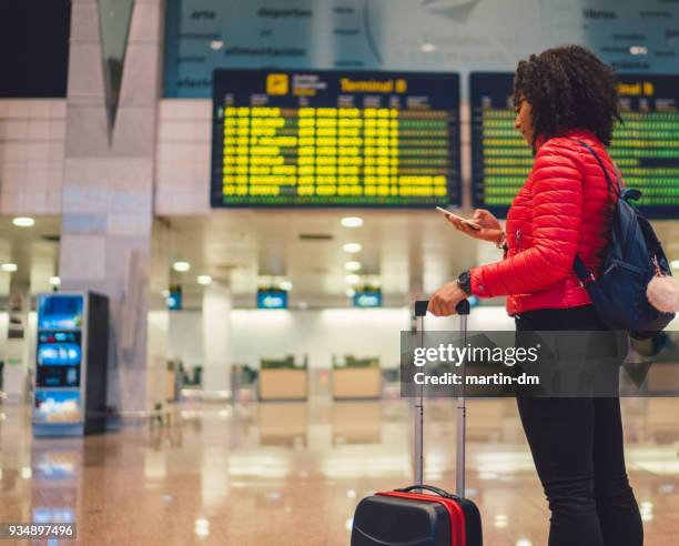 young mixed race tourist woman checking for flight at airport - heathrow airport stock pictures, royalty-free photos & images