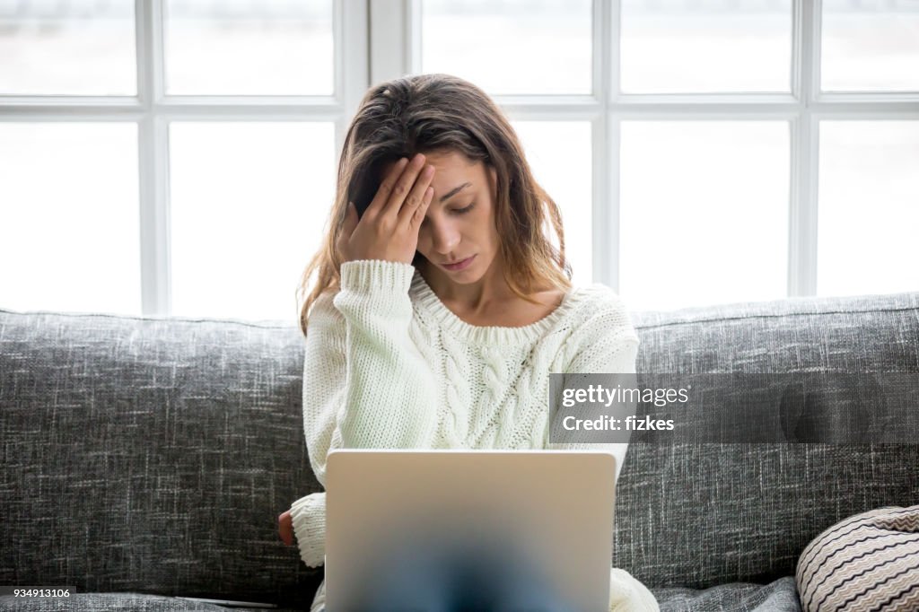 Frustrated woman worried about problem sitting on sofa with laptop