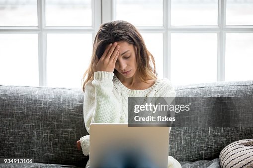 Frustrated woman worried about problem sitting on sofa with laptop Frustrated woman worried about problem sitting on sofa with laptop