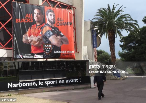 Man walks past a poster of the French rugby club RCNM at the Parc des Sports stadium in Narbonne, southern France, on March 15, 2018. / AFP PHOTO /...