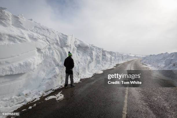 Man stands beneath a huge snow drift on a road in the Pennines on March 20, 2018 in Allenheads, England. Winter conditions are persisting in some...