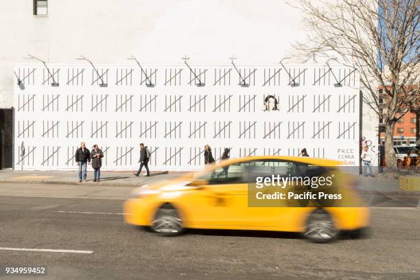 Yellow taxi rides in front of mural painted by anonymous British street artist Banksy to protests imprisonment of Zehra Dogan of Turkey on East...