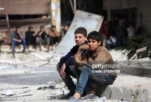Syrian youths sit on the kerb of a street in the Eastern Ghouta town of Kafr Batna, on the northeastern outskirts of Damascus, on March 20, 2018....