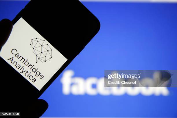 In this photo illustration the logo of the strategic communication company "Cambridge Analytica" is seen on the screen of an iPhone in front of a...