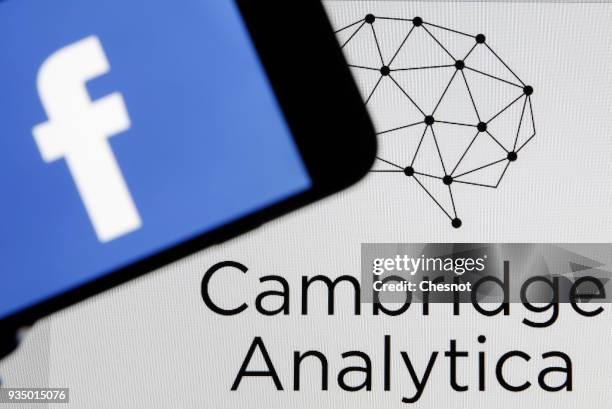 In this photo illustration the Facebook logo is seen on the screen of an iPhone in front of a computer screen showing a Cambrige Analytica logo on...