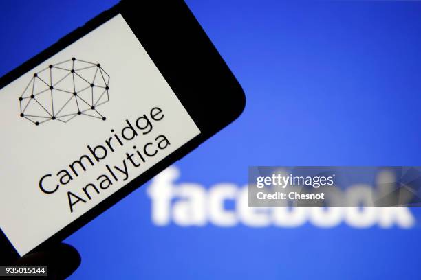 In this photo illustration the logo of the strategic communication company "Cambridge Analytica" is seen on the screen of an iPhone in front of a...