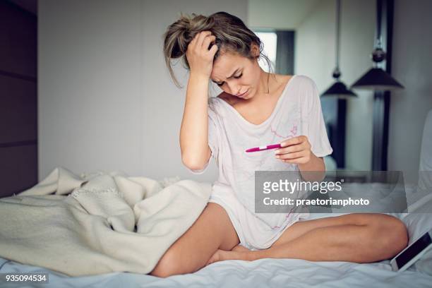 shocked young girl with unwanted pregnancy looking the test in the bedroom - pregnancy test stock pictures, royalty-free photos & images
